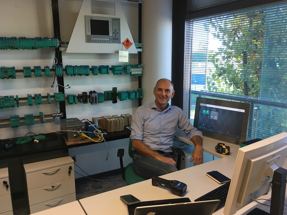 Giovanni, Global Technical Support Manager, sits behind his desk in the office. Many Pepperl+Fuchs products can be seen behind him.