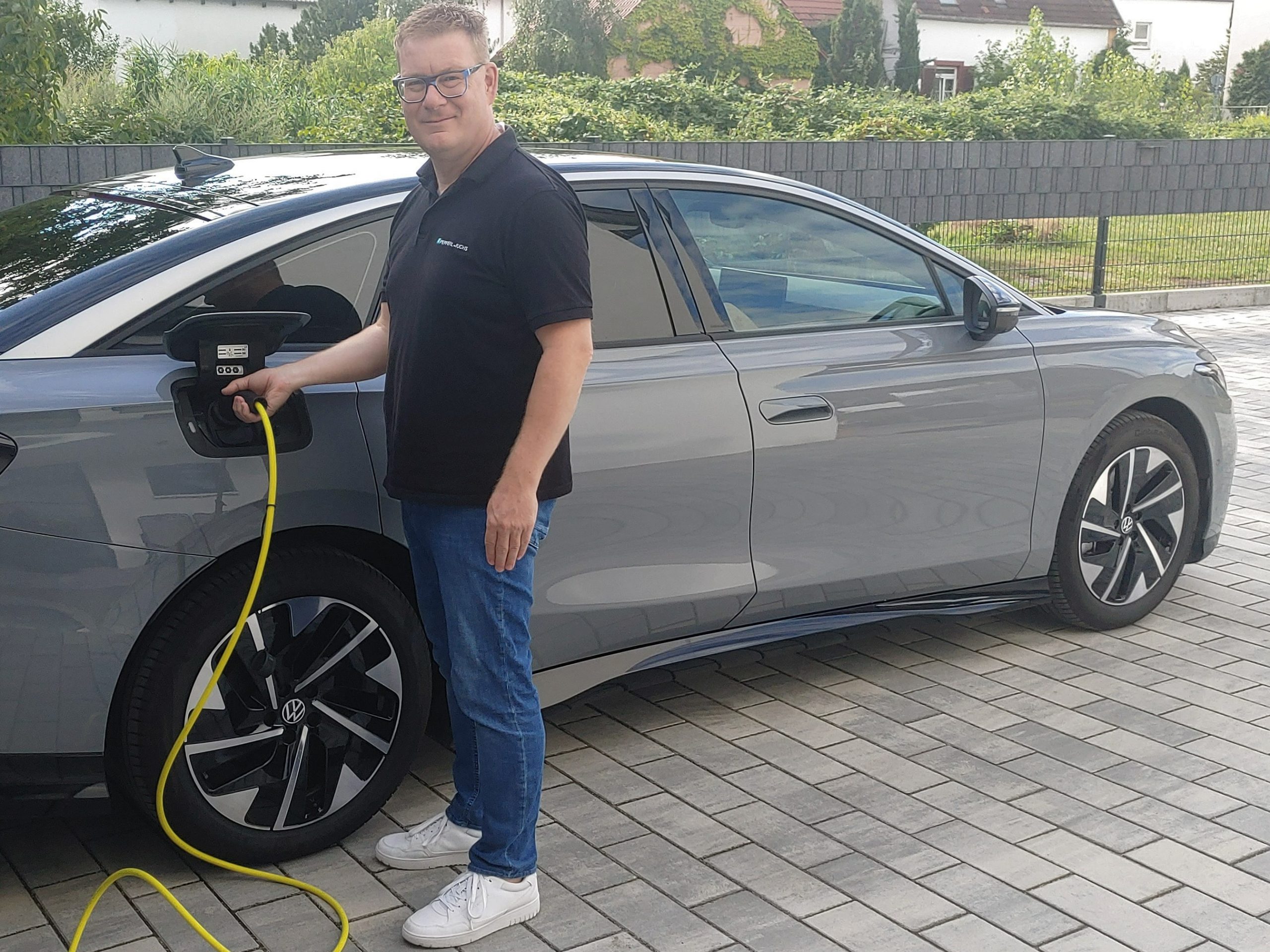 Andreas drives an e-car as a company car at Pepperl+Fuchs. Here he is standing in front of his silver-colored electric car and is currently hanging it on the charging station.