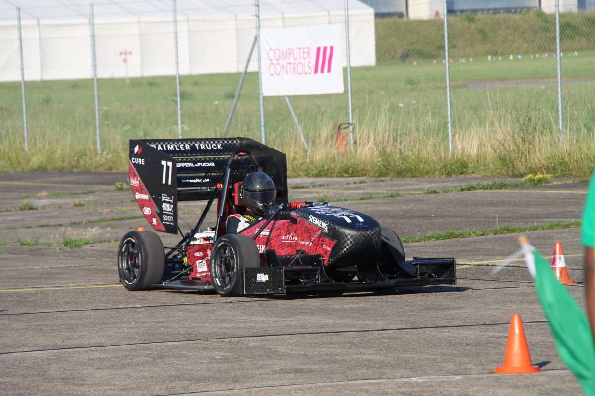 A student Formula One racer sits in the electric self-built racing car from the CURE Association. The care is on a racetrack.