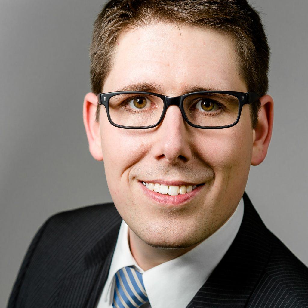 Profilbild von Dr. Jörg Nagel, Leiter Neoception. Er trägt einen Anzug mit blau, silberner gestreifter Krawatte, eine Brille und lächelt in die Kamera.