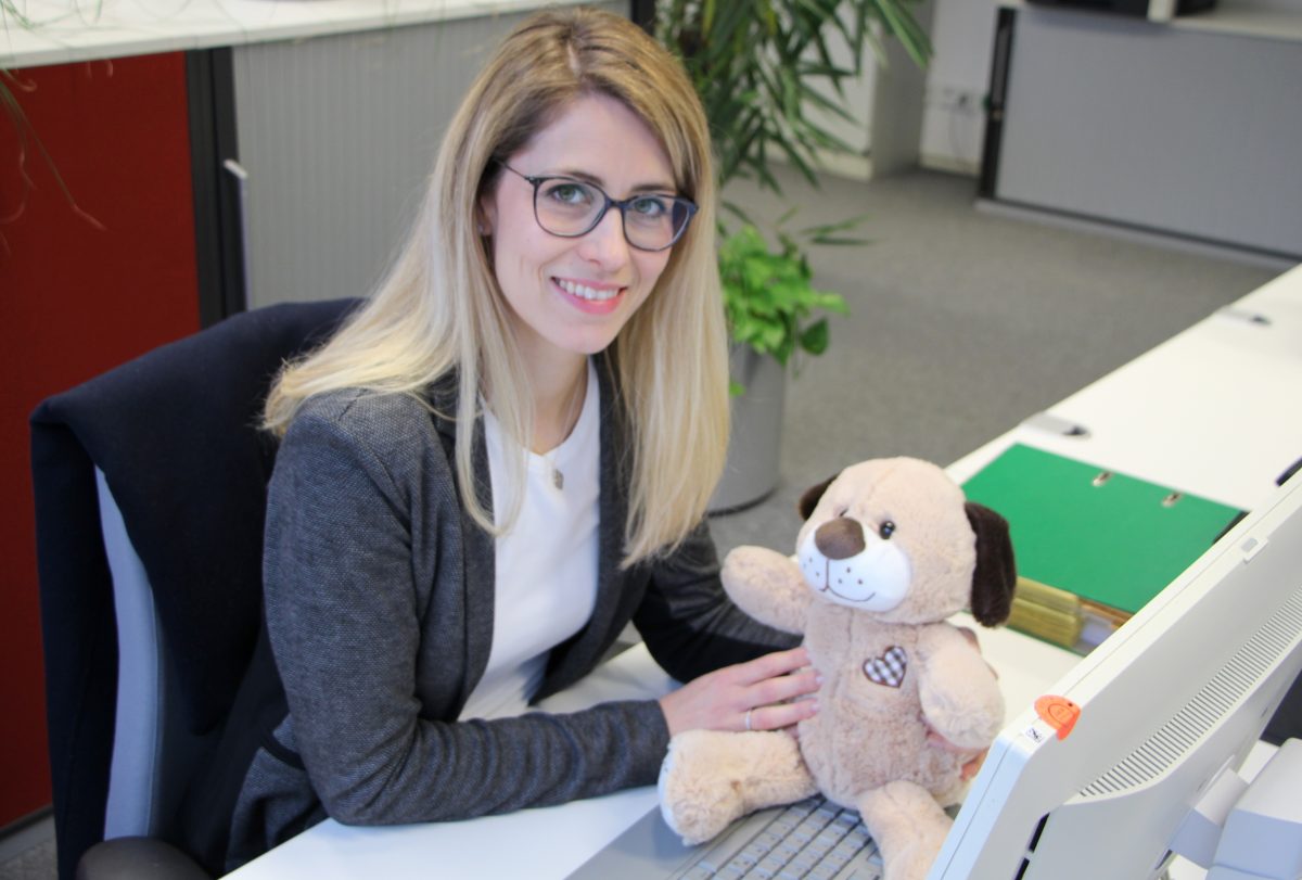 Mascha sitzt an ihrem Arbeitsplatz bei Pepperl+Fuchs. Sie hält einen Teddybären in den Händen und lächelt in die Kamera.