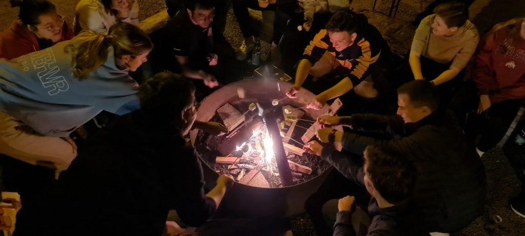 Die neuen Auszubildenden und dual Studierenden sitzen abends um ein Lagerfeuer herum und grillen Marshmallows.