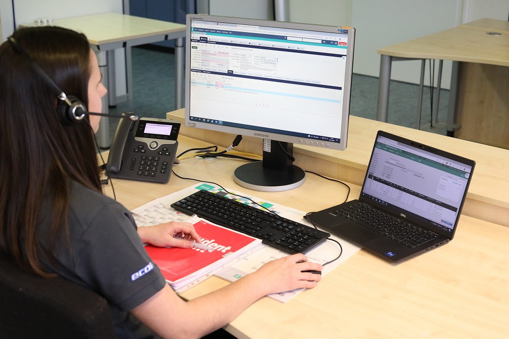 Theresa, Industriekauffrau bei ECOM Instruments, an ihrem Arbeitsplatz. Sie sitzt an ihrem Schreibtisch vor ihrem Computer mit Blick zum Bildschirm.