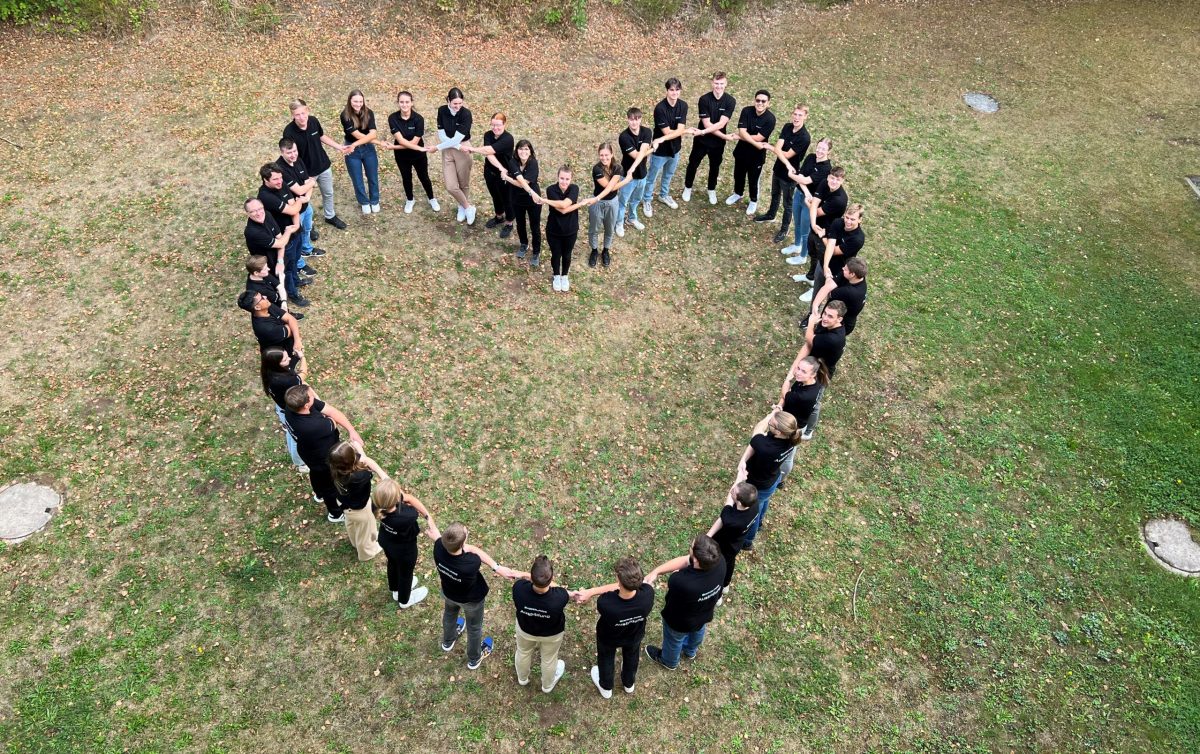 Bild aus der Vogelperspektive: Die 19 Auszubildenden und dual Studierenden von Pepperl+Fuchs stehenauf einer Wiese und bilden die Form eines Herzens.
