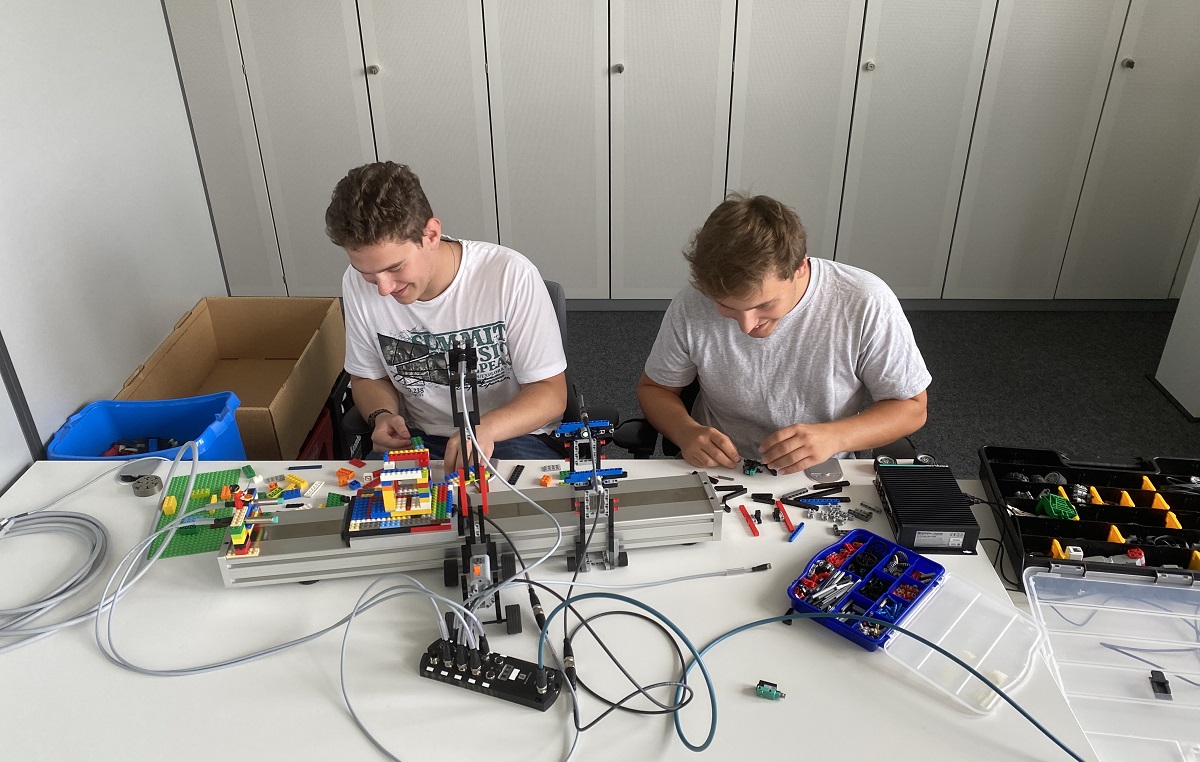 Aaron und Fabian, die beide das Studium Elektrotechnik bei Pepperl+Fuchs absolvieren, sitzen am Tisch und bauen an ihrer Konstruktion. Auf dem Tisch liegen verschiedenste Materialien, unter anderem auch die Legobausteine.