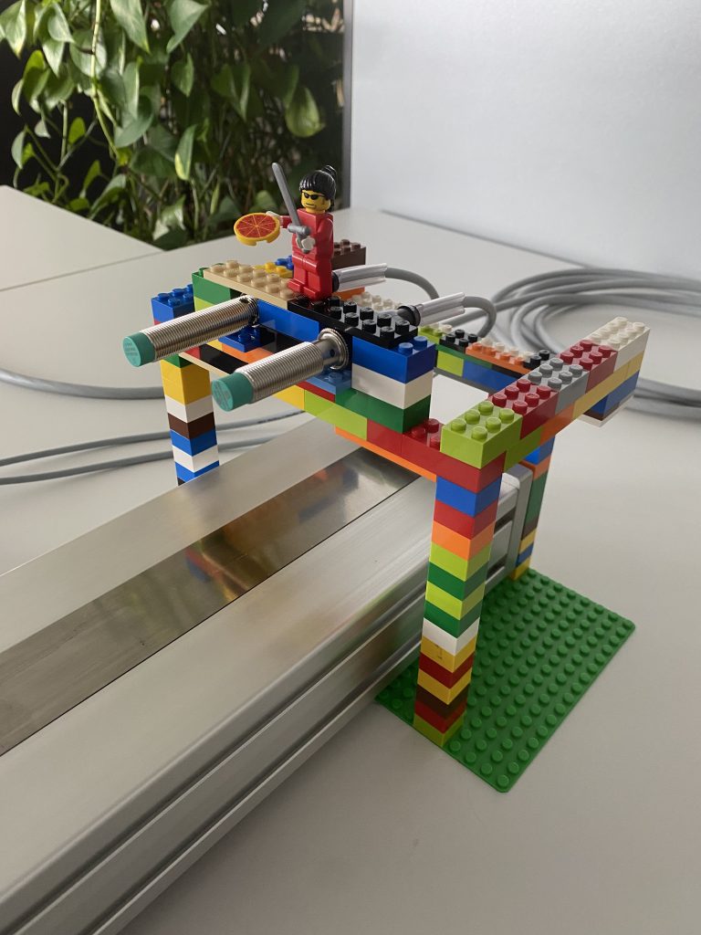 Detailaufnahme auf eine Halterung mit Legobausteinen. Die Legobausteine sind bunt und auf dem Bau steht aus Spaß ein Legomännchen mit einer Pizza in der Hand.