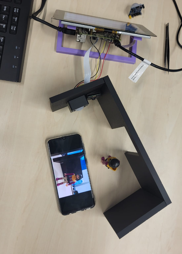 Wettbewerb "Kreative Köpfe": Bild aus der Testphase mit einem keinen Versuchsaufbau. Zu sehen ist ein Smartphone, welches neben einem selbstgebauten Modell liegt, welches den Eingangsbereich darstellen soll. Daneben steht eine Playmobilfigur.