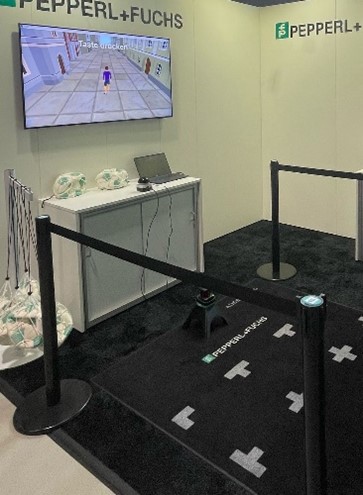 Blick auf das R2000 Pin Ball Detection Spiel am Messestand von Pepperl+Fuchs bei der Jobs for Future. Man sieht einen Bildschirm mit der Person darauf, ein Steuerpult und einen schwarzen Teppich mit Markierungen.